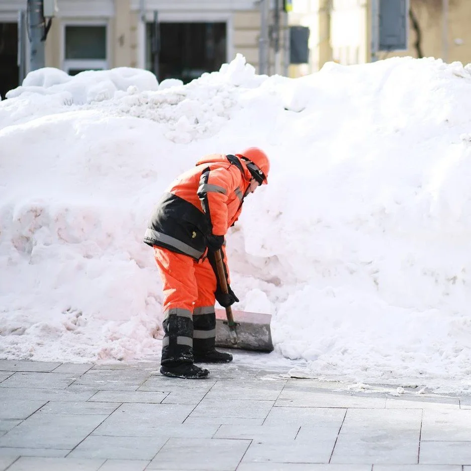 Snow removal crew member shoveling a heavy snow pile from a commercial sidewalk in Seattle, WA