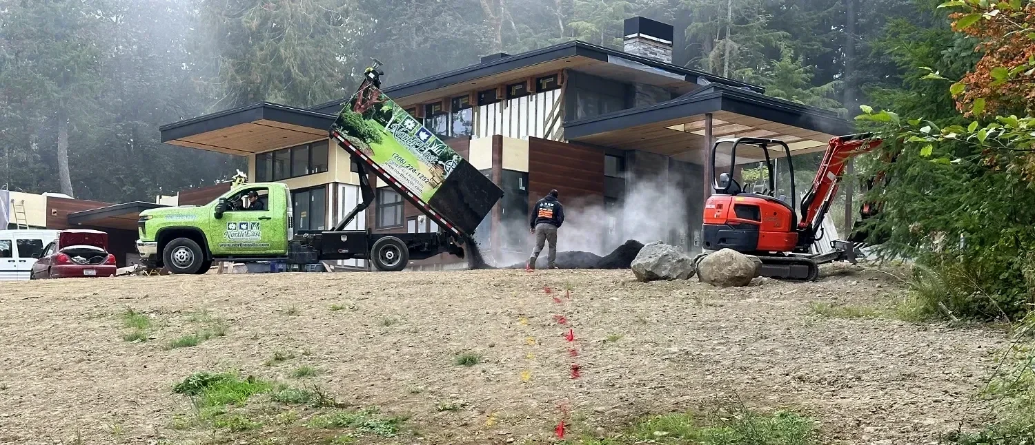 Landscape construction project in Redmond, WA with material delivery, excavation equipment, and crew preparing a residential outdoor space