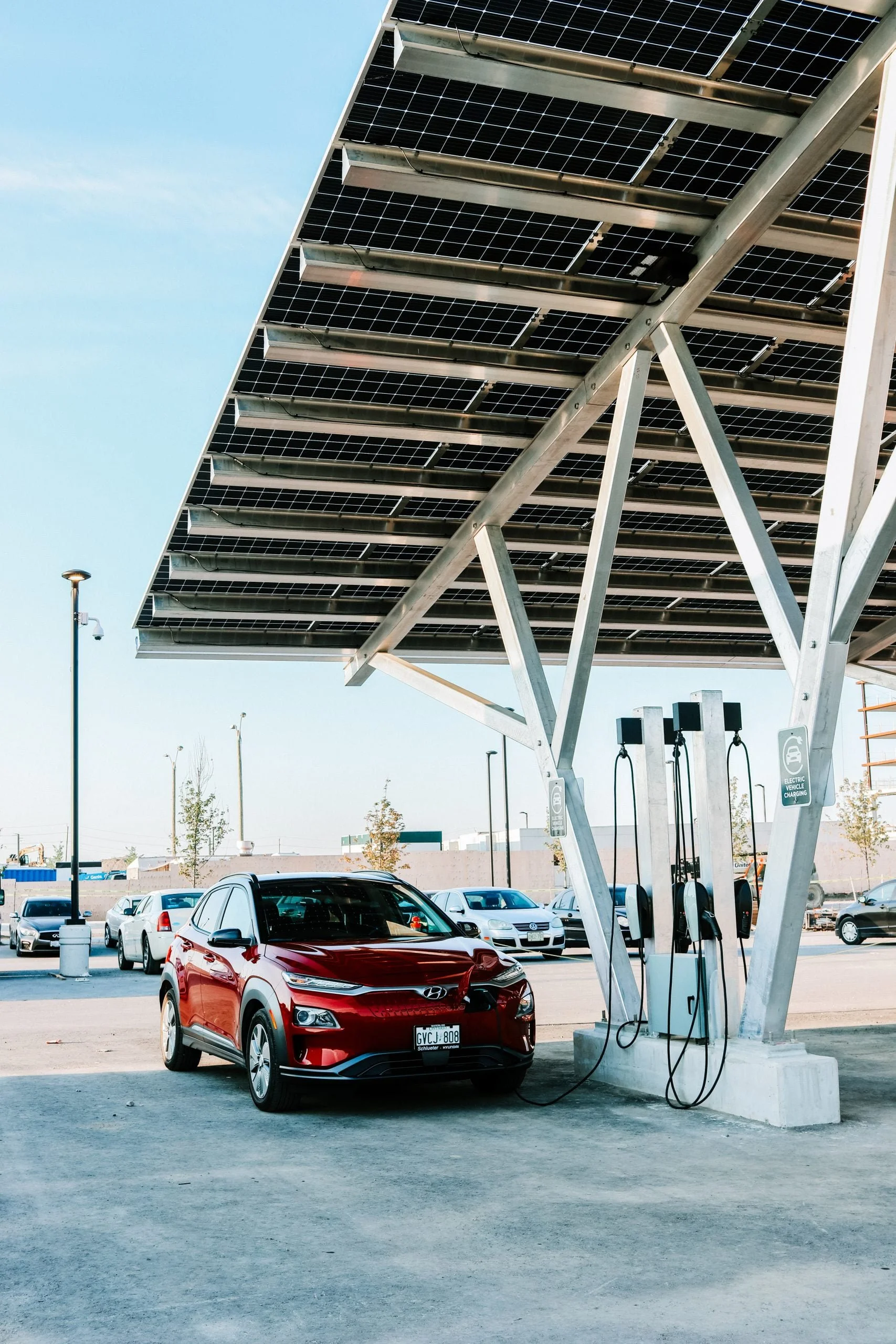 VCT Group solar carport system at Pickering Casino Resort. A red electric vehicle parked at a solar-powered charging station in a parking lot, with solar panels overhead.