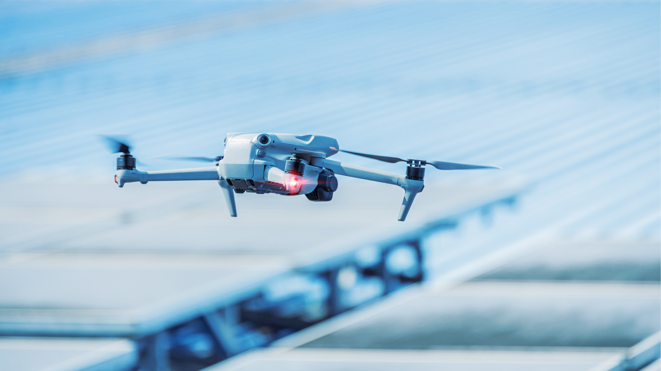 A drone flying through the air over a solar panel installation with a blue sky background.