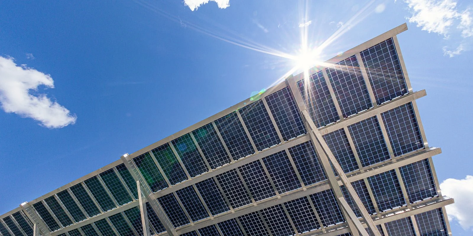 Solar panels mounted on a building's roof with sunlight shining brightly and a blue sky with a few clouds. VCT Group solar carport system.