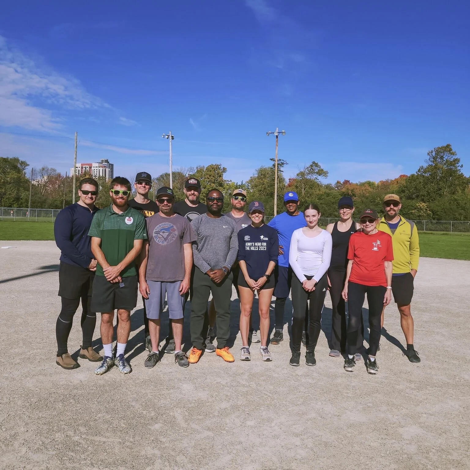 VCT Group team of employees standing on a field with a chain-link fence, trees, and blue sky in the background.