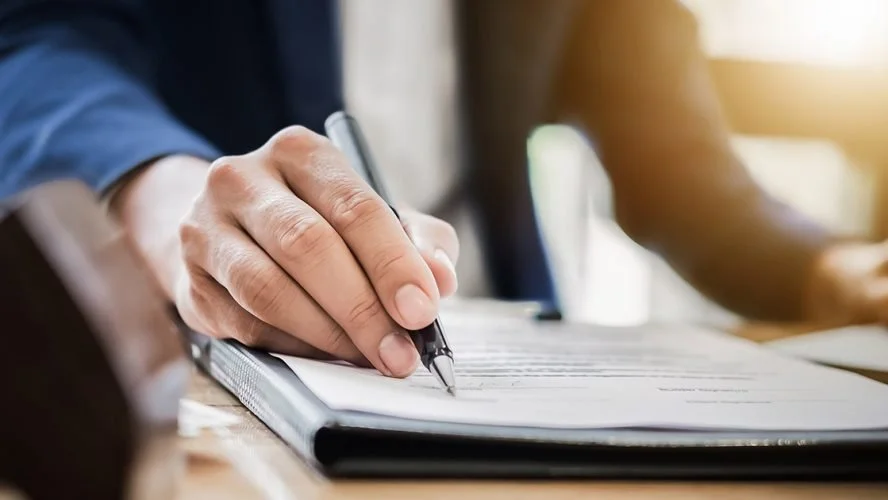 A person signing a document with a pen on clipboard