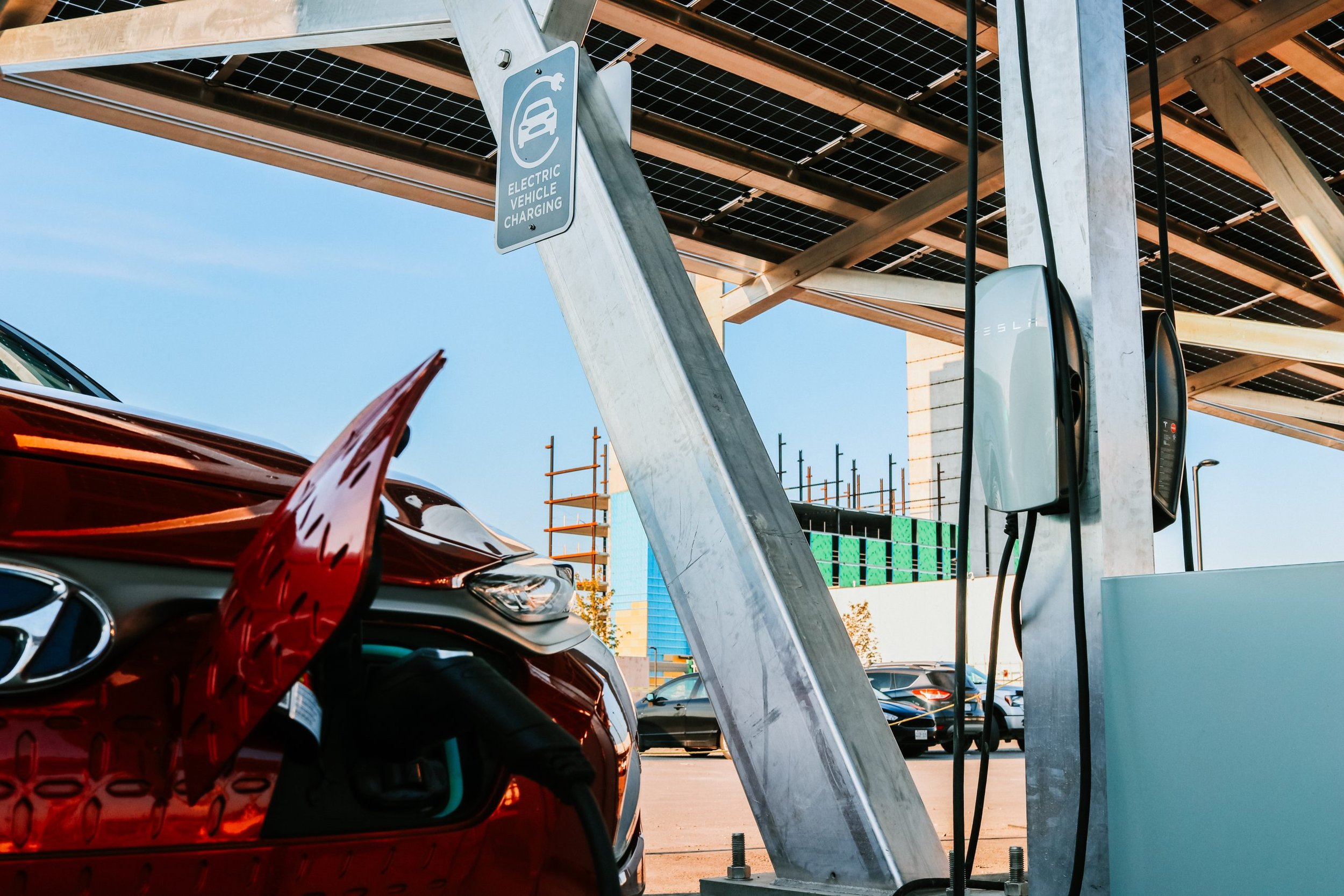 VCT Group solar carport system at Pickering Casino Resort. Electric vehicle charging station with a red car plugged in, under a solar panel-covered structure, in an outdoor parking lot.