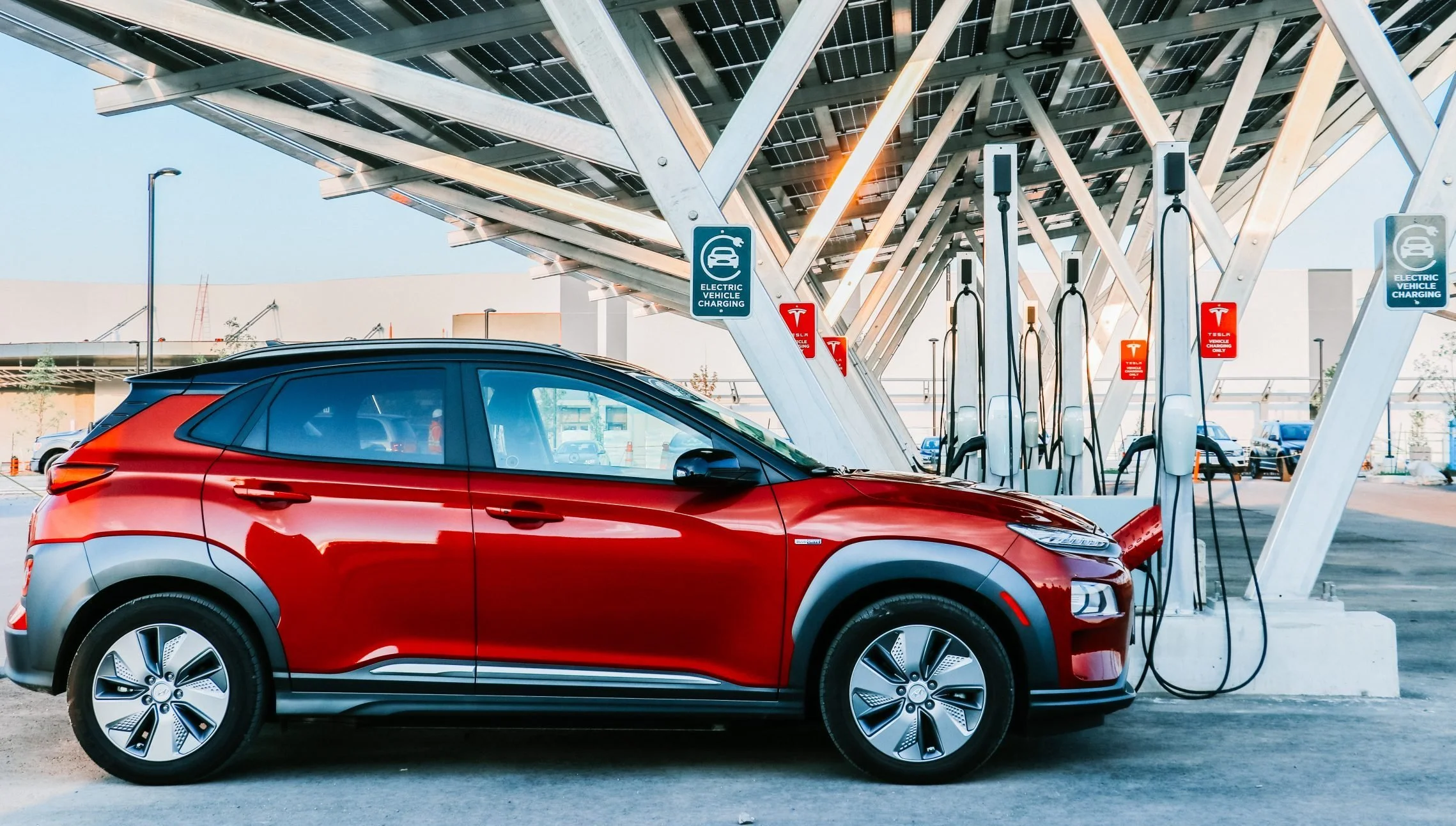 Red electric vehicle charging at a charging station under a VCT Group solar carport system.