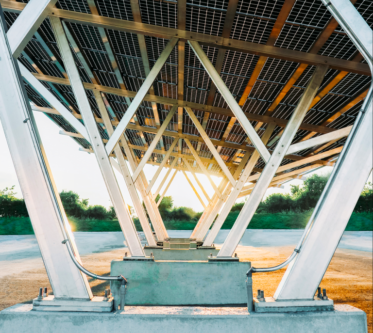 Underneath view of a solar carport array mounted on metal supports with a sunset in the background.