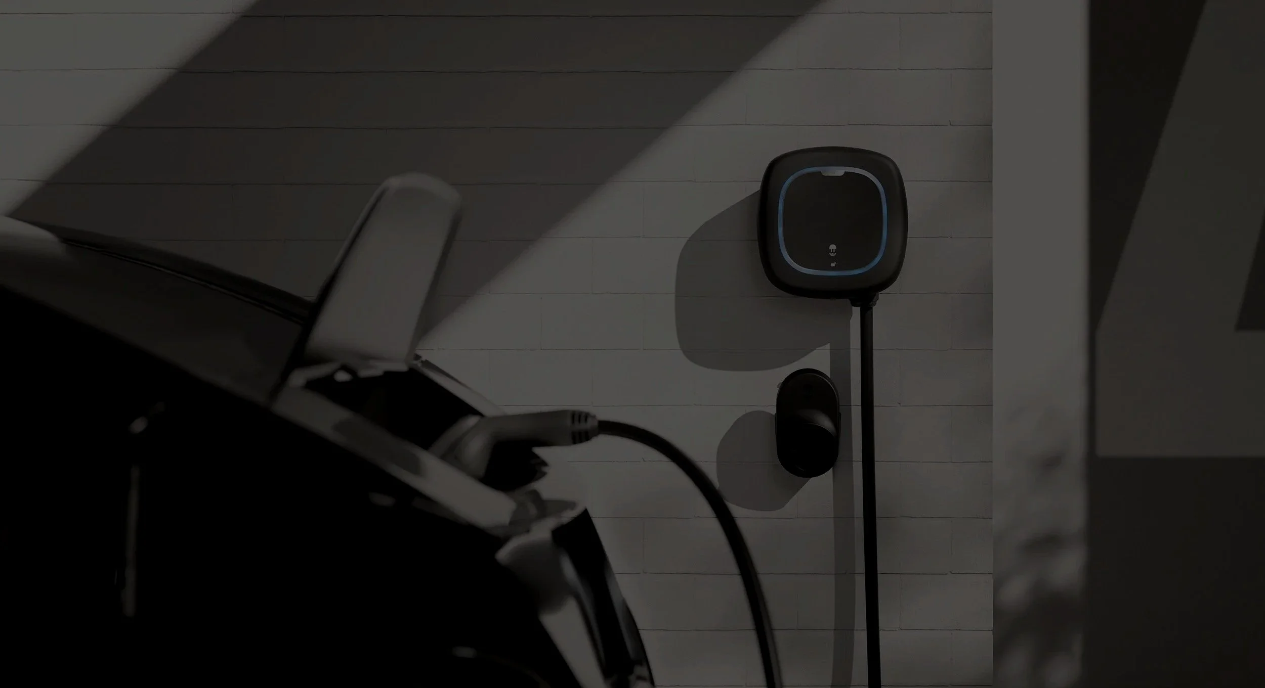 Electric vehicle charging station with a charging cable plugged in, mounted on a white brick wall in an indoor setting.