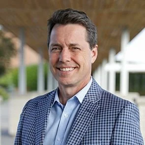 Marc Ayotte, Head of College HSC in a blue checkered blazer outdoors with a modern building in the background.