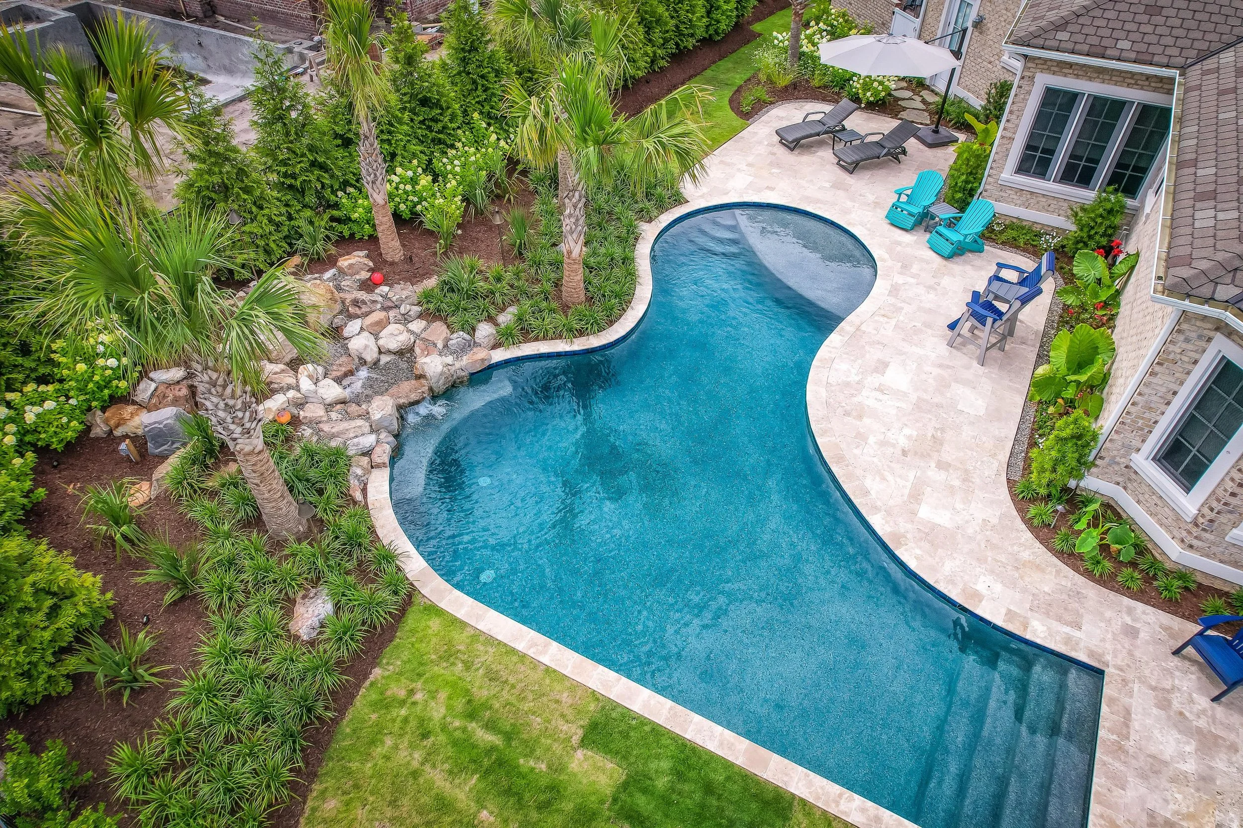 Poolscape tying into a large outdoor living area, created by a pool builder near me in Wilmington, NC with layered landscape design