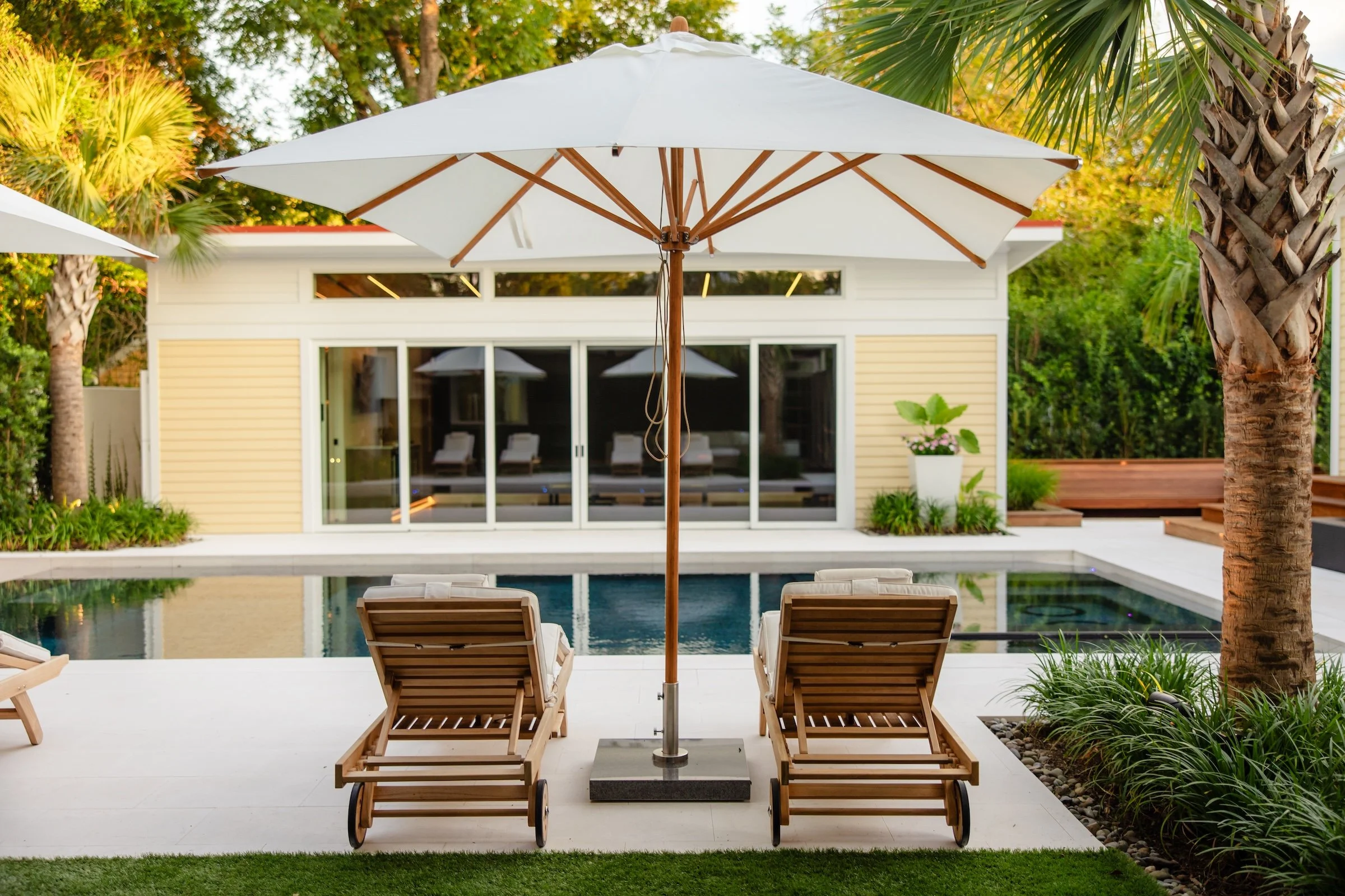 White umbrella over two wooden lounge chairs beside inground pool