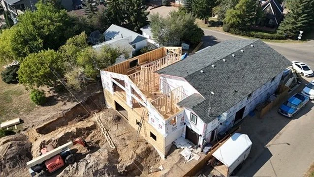 Aerial image of a new custom garage in an established neighbourhood, with one half being partially completed roof and siding, and the other half still in the framing stage.