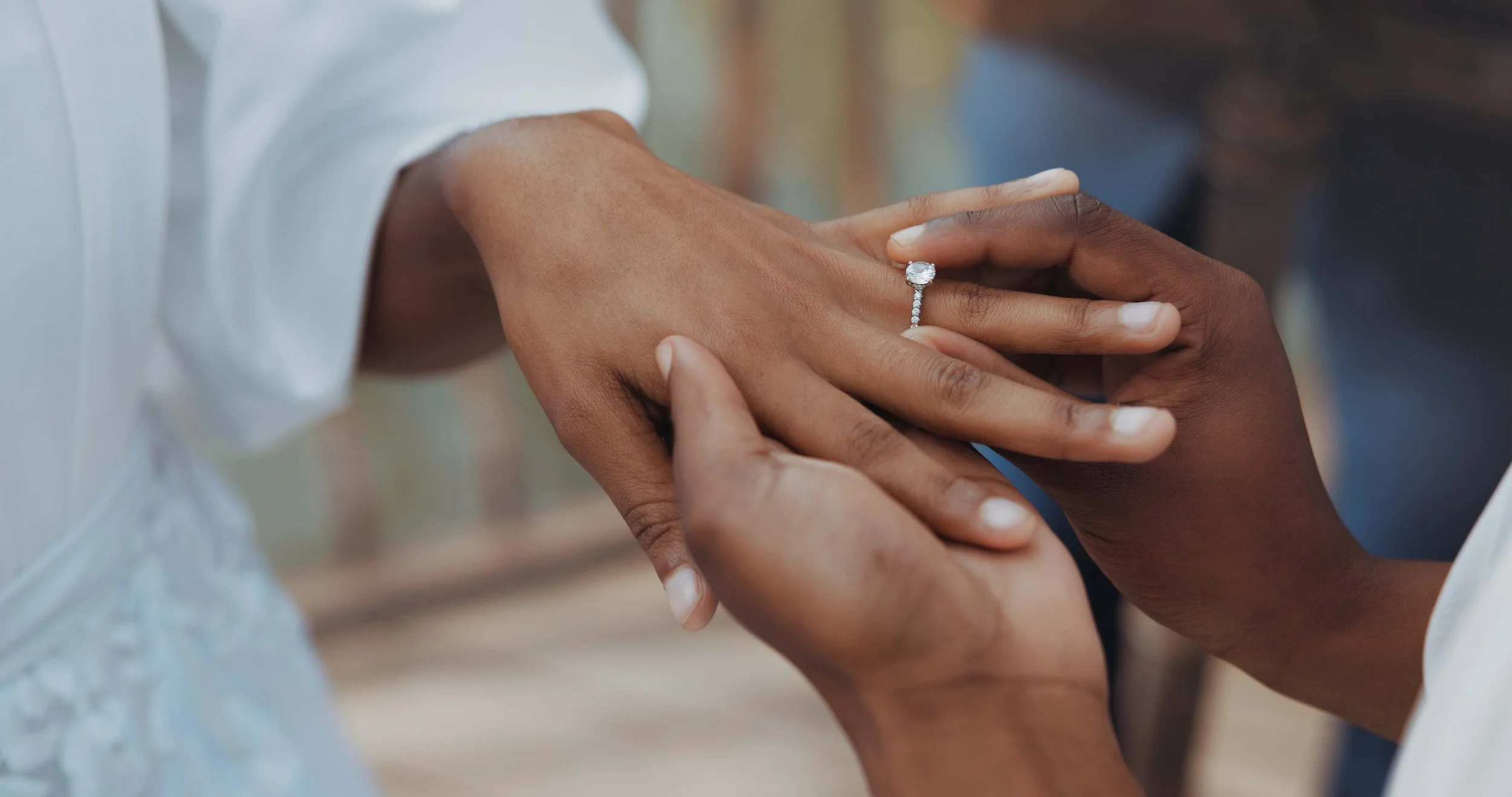 Two hands, one with a diamond engagement ring, are holding each other.
