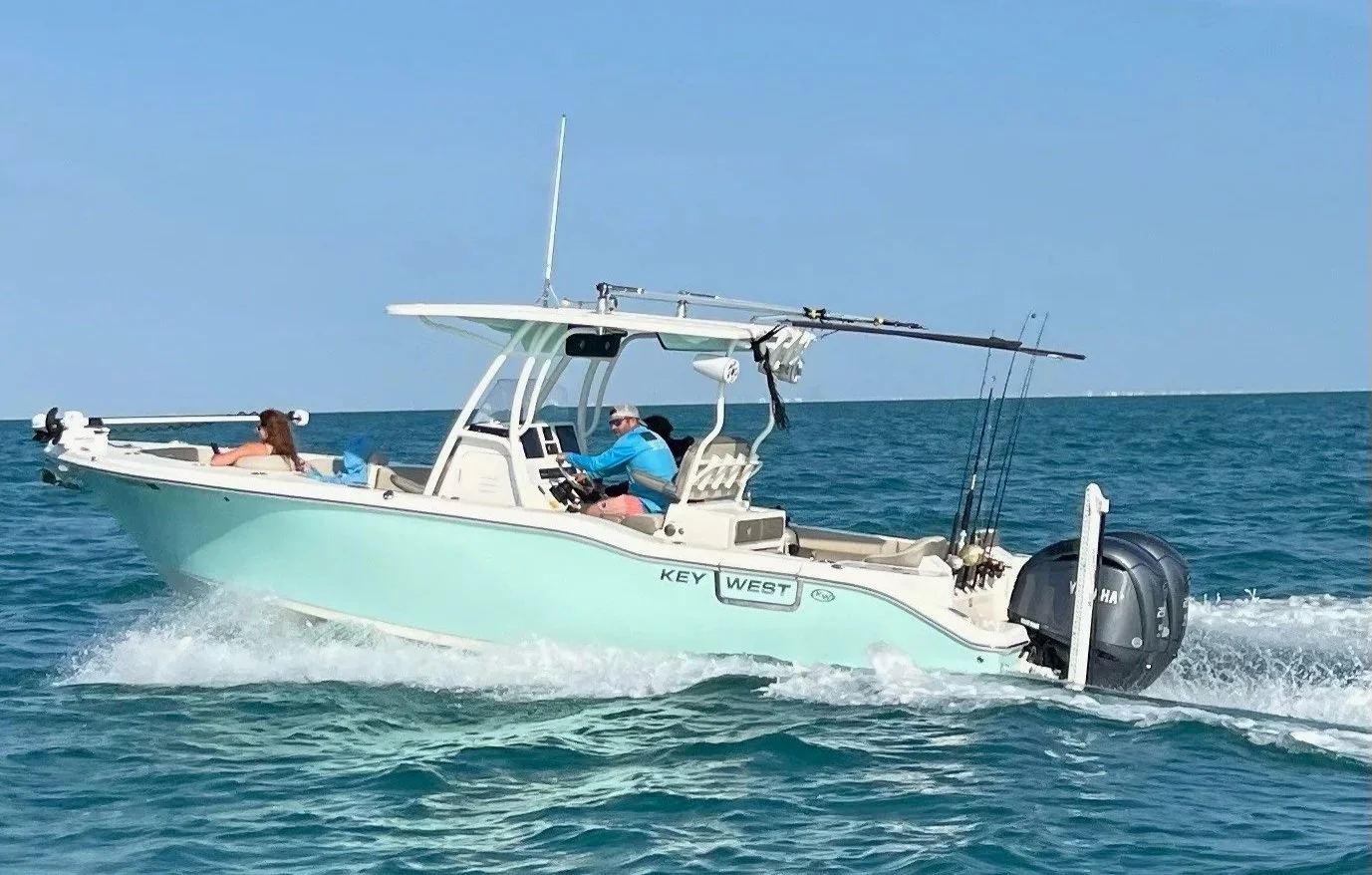 A small powerboat with two people on board, one steering and the other lying down, on clear blue water under a sunny sky.