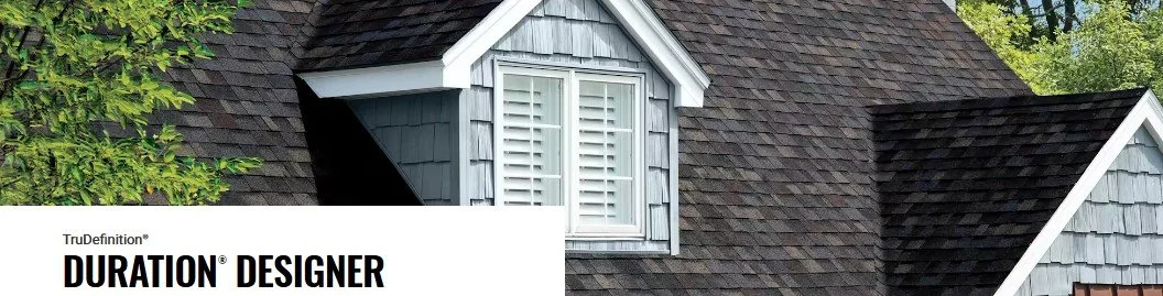 Close-up of a house roof with gray shingles and a dormer window with white shutters, surrounded by green trees.