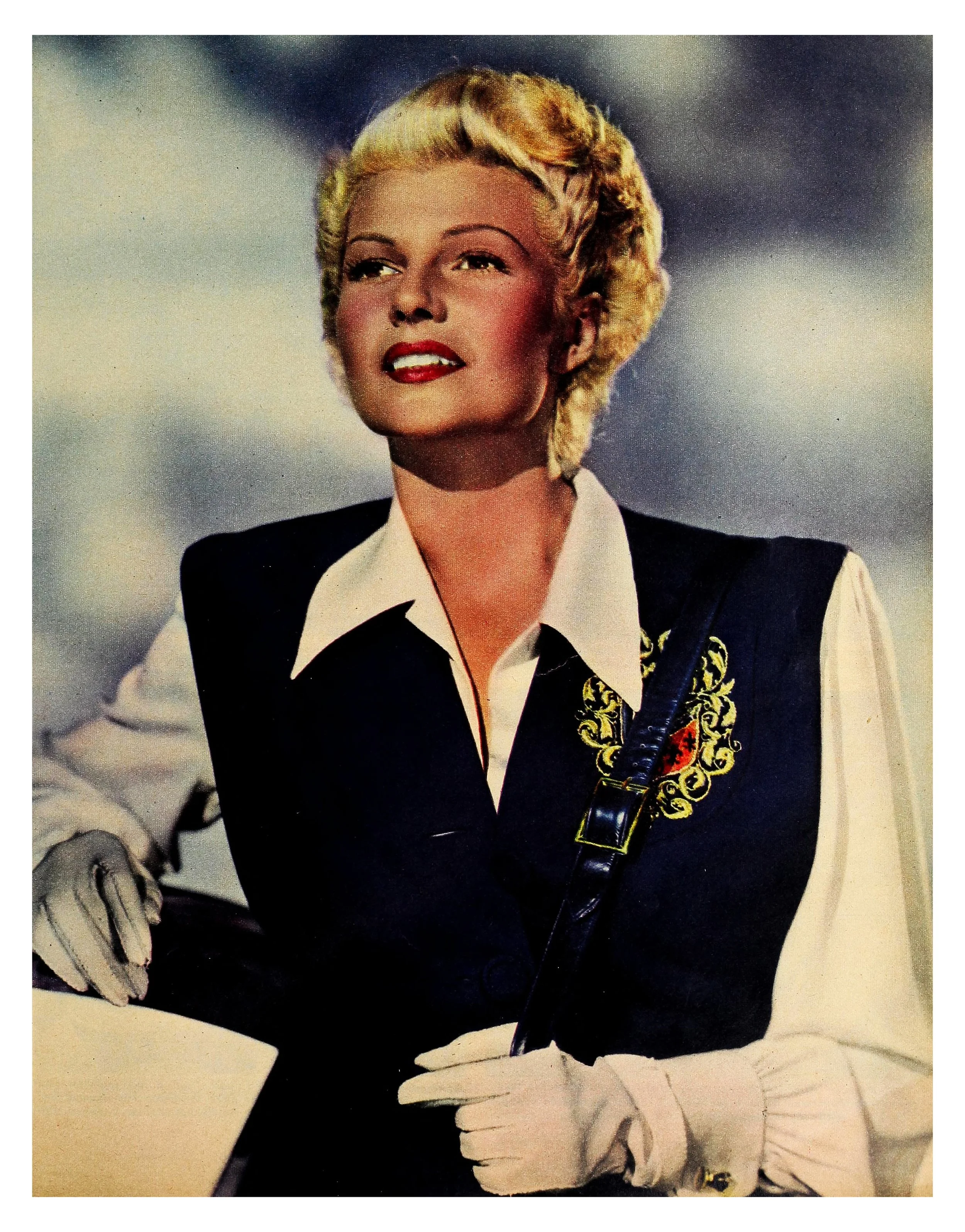 A woman with blonde hair styled in elegant waves, wearing a vintage black vest with gold embroidery, a white blouse, white gloves, and holding a black handbag, standing against a cloudy sky background.