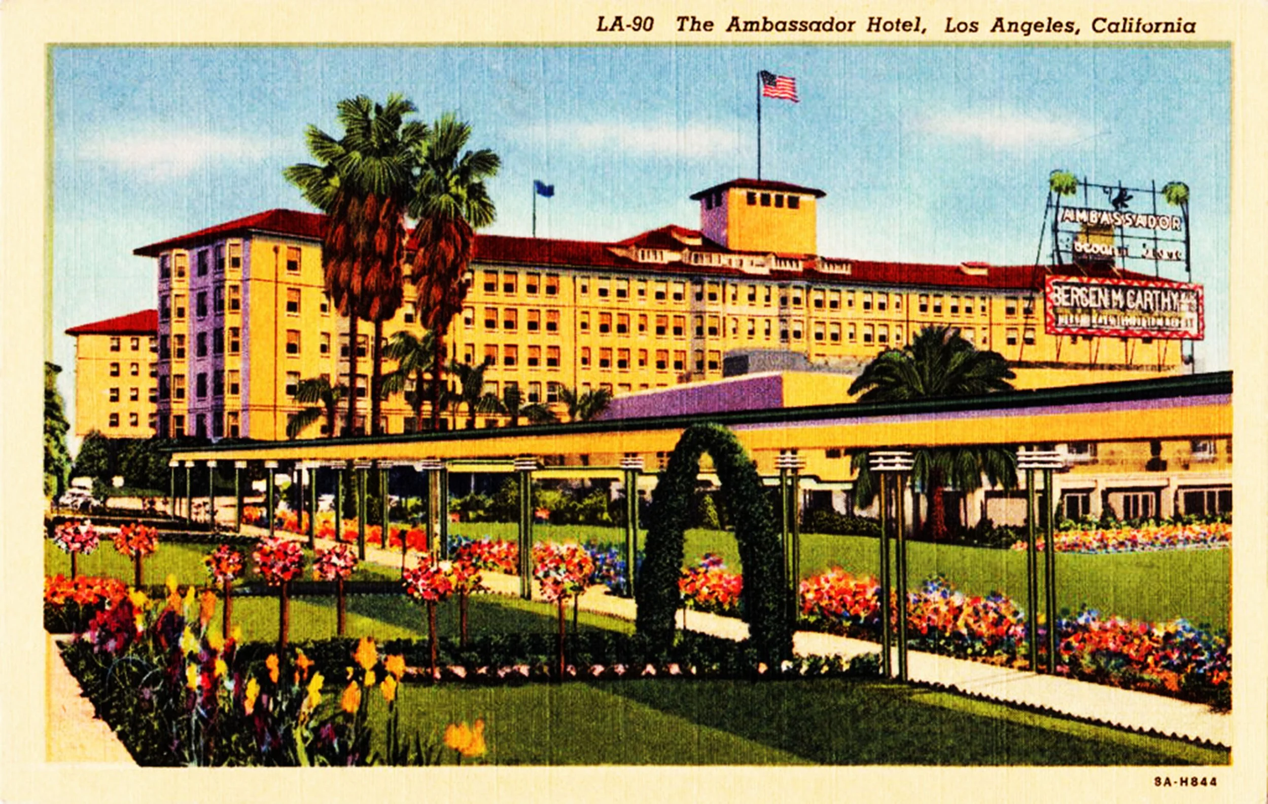 Illustration of the Ambassador Hotel in Los Angeles, California, with a colorful garden and palm trees in front, and a sign with the hotel name in the background, under a blue sky.