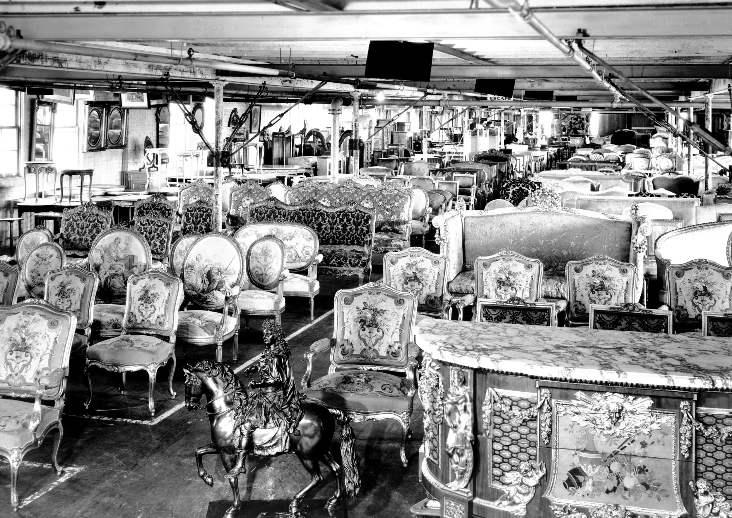 A large indoor space filled with antique furniture, including ornate chairs, sofas, and tables, with a vintage carousel horse in the foreground.