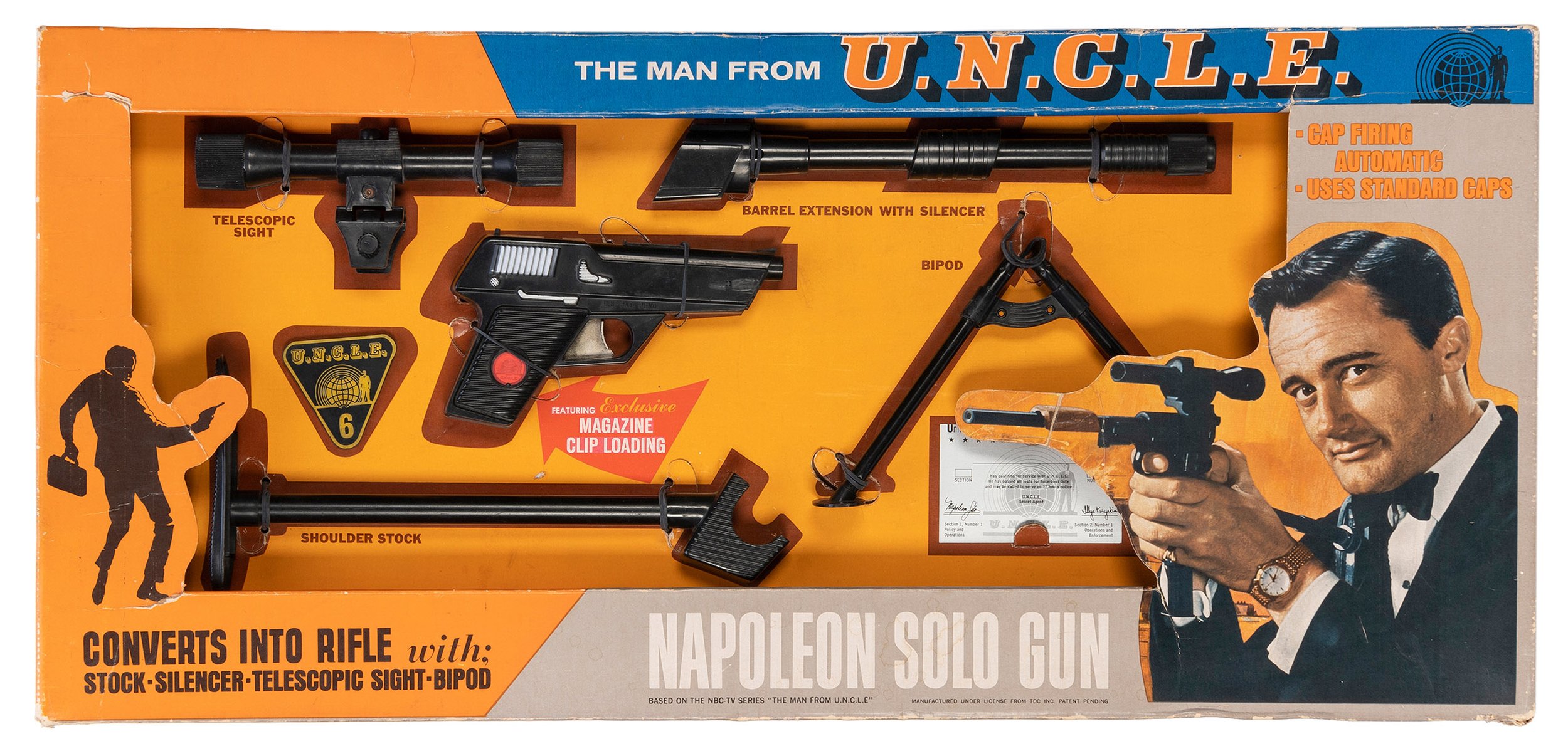 Vintage toy gun set in packaging with a 1950s man holding a gun, labeled as U.N.C.L.E. Napoleon Solo Gun, including parts like a telescopic sight, barrel extension, bipod, shoulder stock, and magazine clip loading feature.