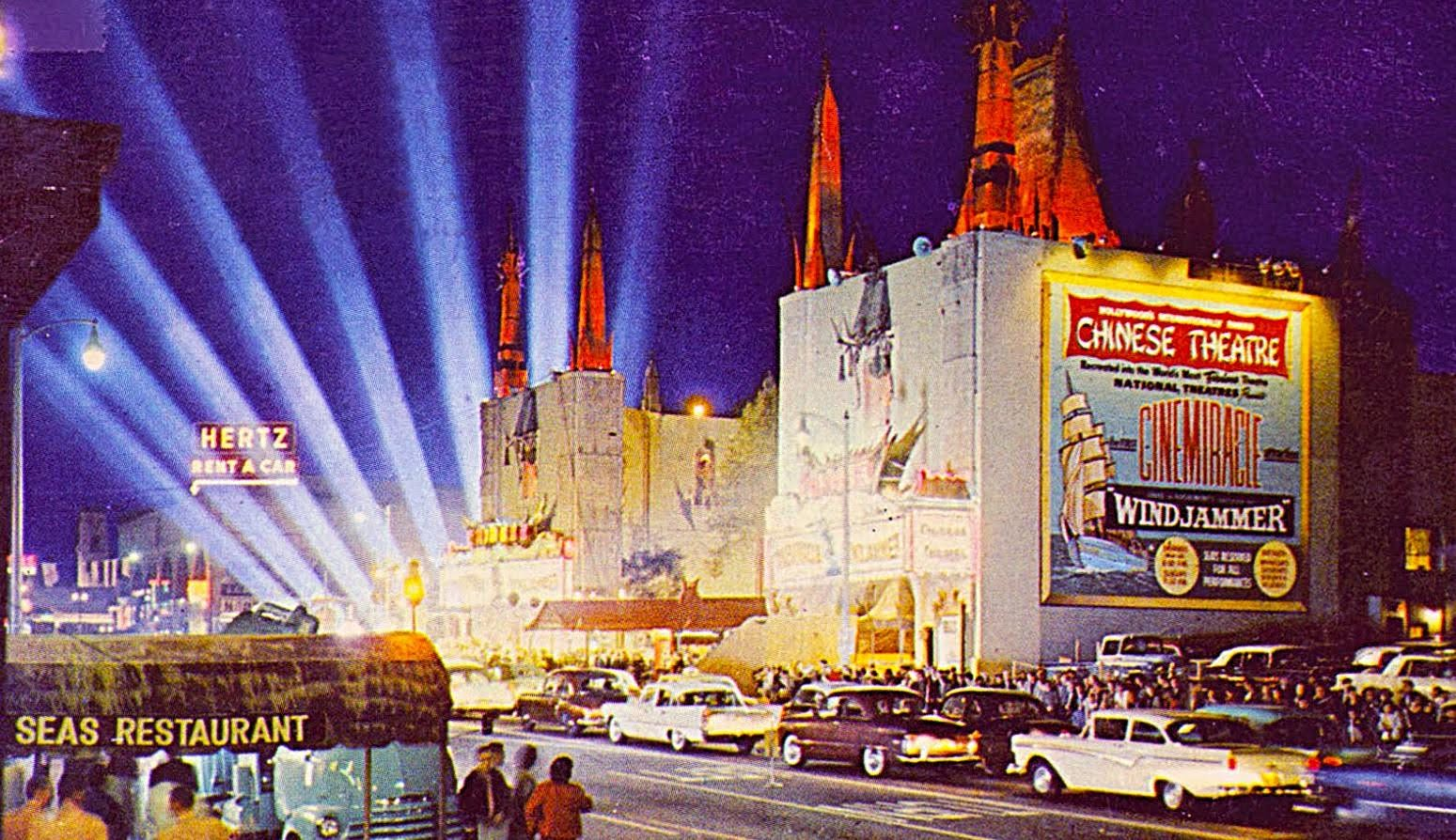 Night scene at the Chinese Theatre with a large movie poster for 'The Chinese Theatre' and 'Wild Jammer,' stage lighting hitting the sky, vintage cars parking and people walking on the street, and a sign for Hertz Rent A Car.