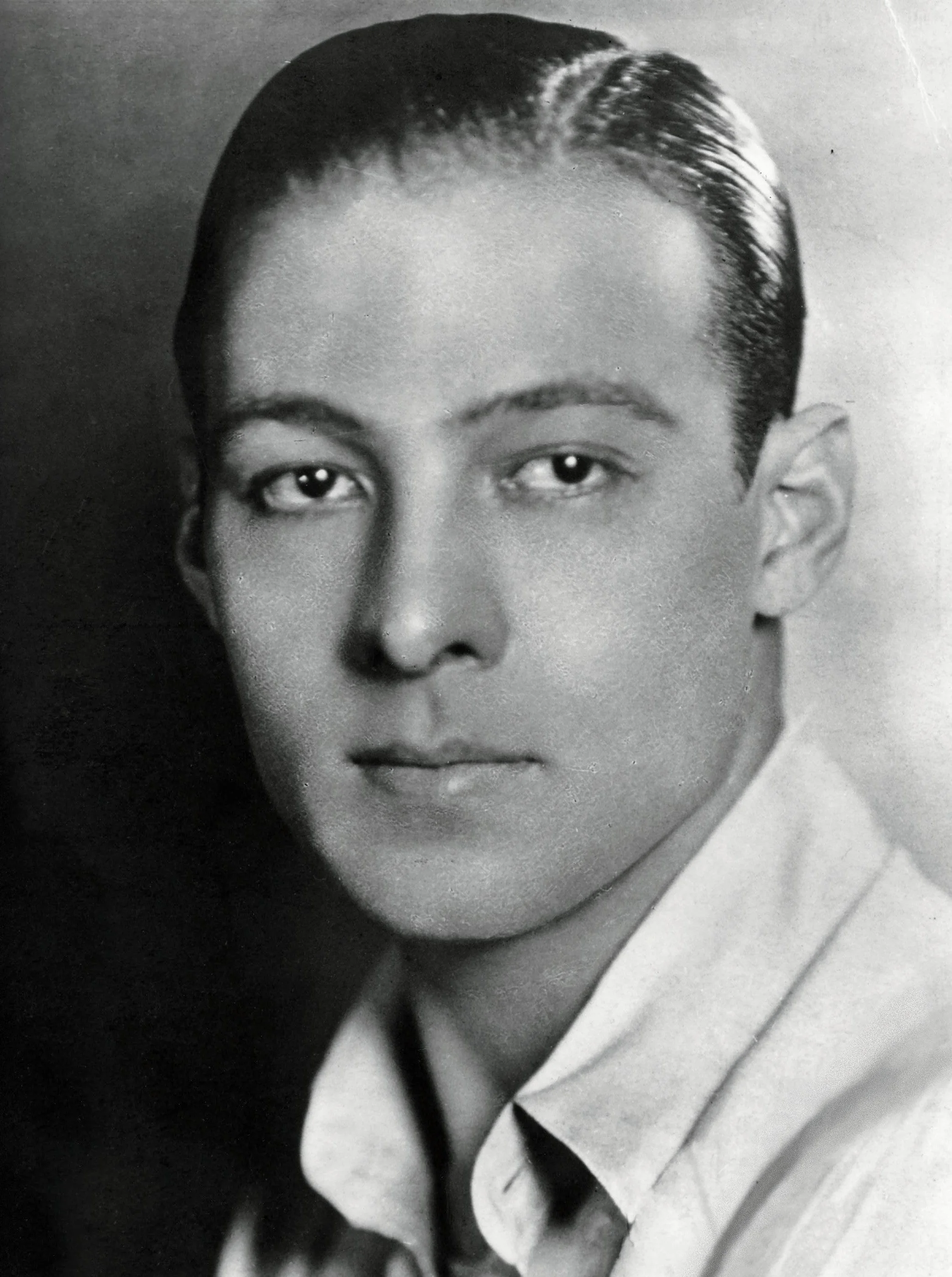 Black and white portrait of a young man with neatly combed hair, wearing a collared shirt, looking directly at the camera with a serious expression.