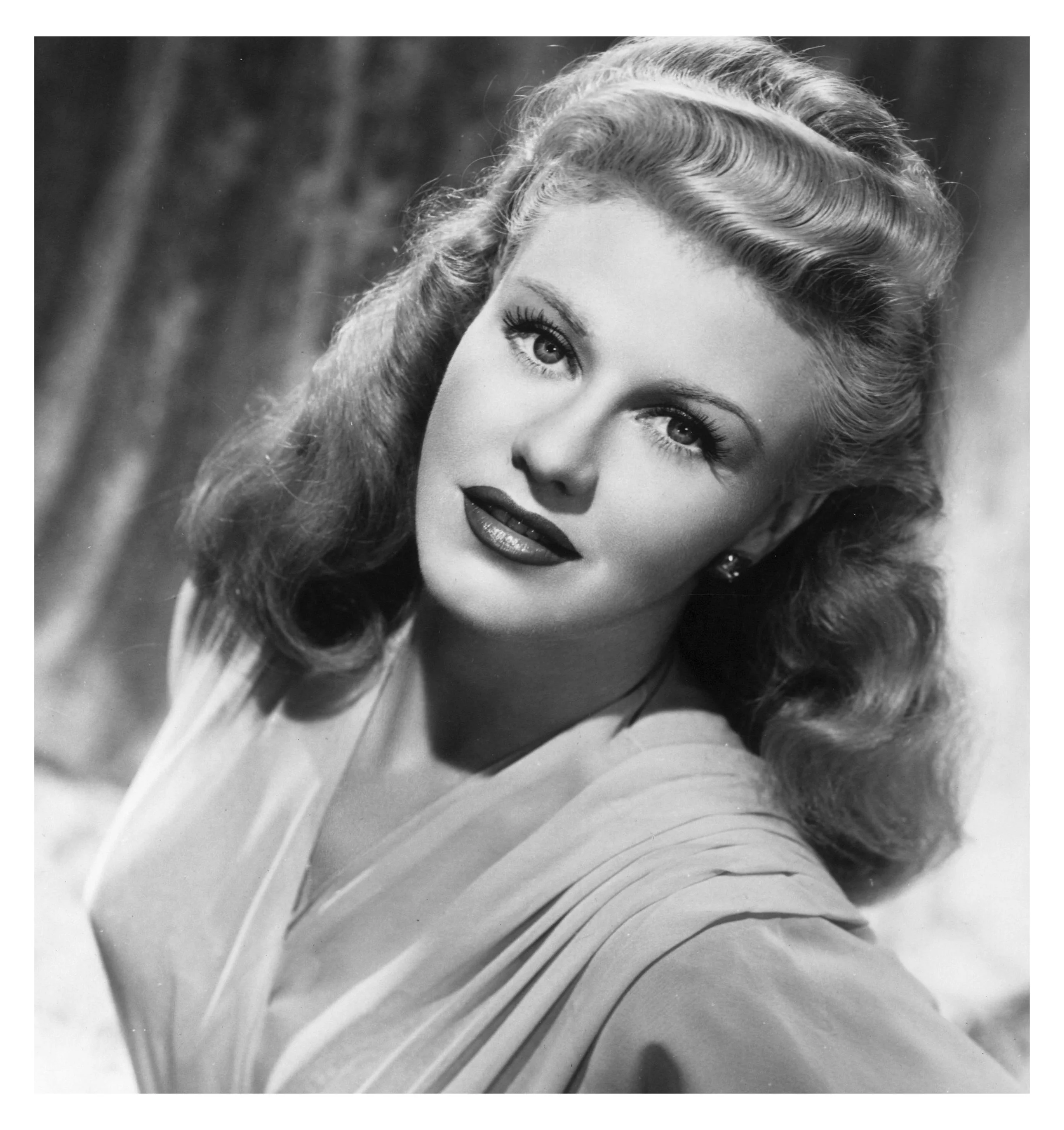 Black and white portrait of a woman with styled wavy hair, wearing earrings and a light-colored top, looking at the camera with a slight smile.