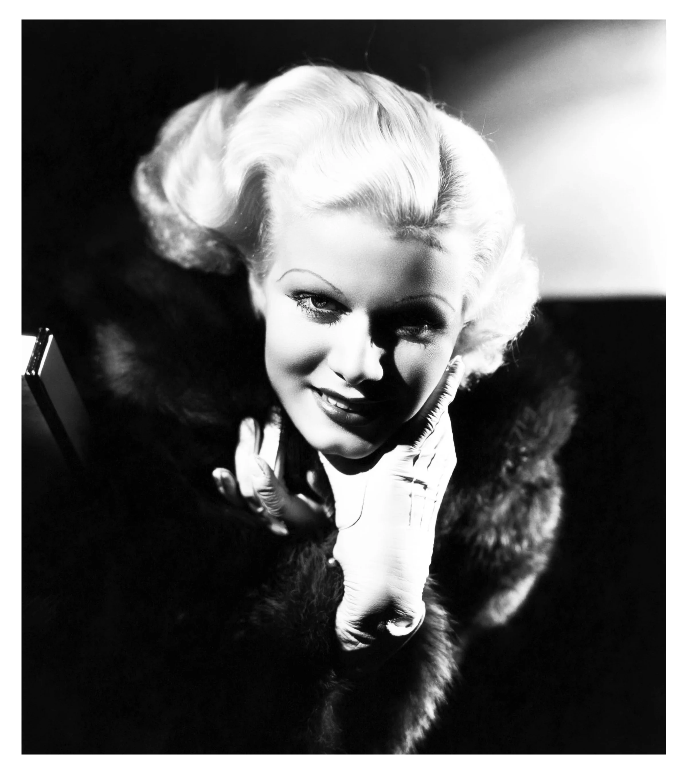 Black and white photograph of a glamorous woman with vintage hairstyle, smiling and resting her face on her gloved hands, wearing a fur stole.