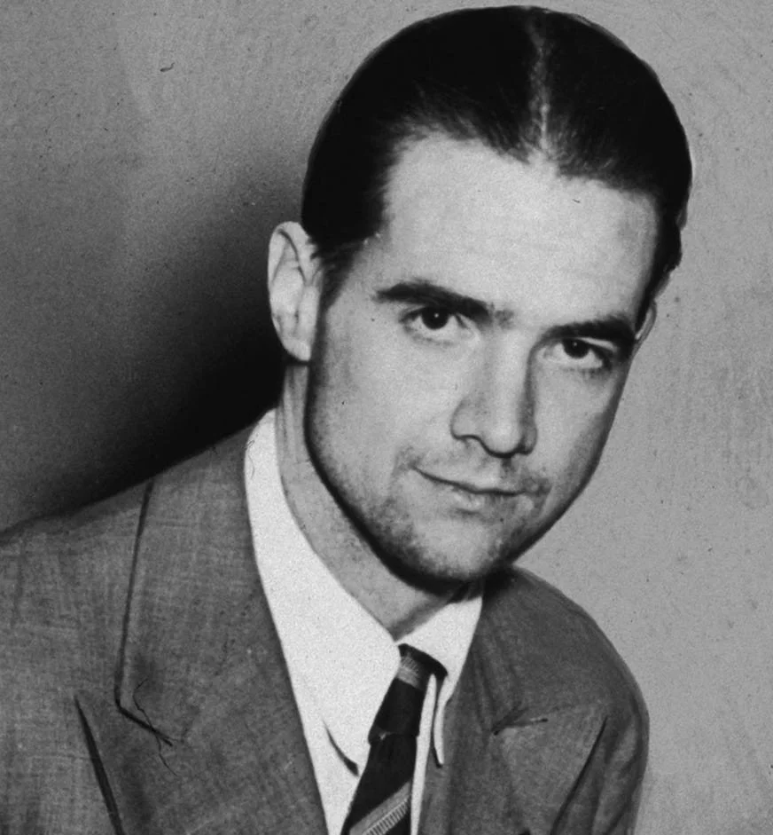 Black and white photograph of a young man with slicked back hair, wearing a suit and tie.
