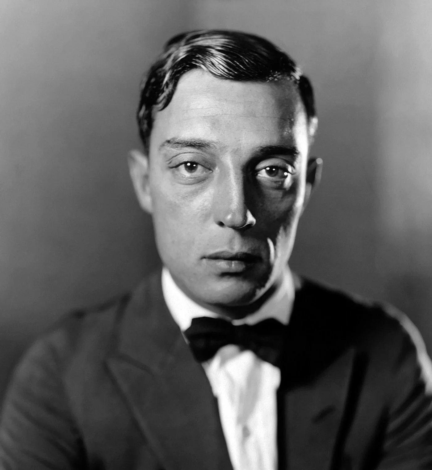 Black and white portrait of a man wearing a tuxedo with a bow tie, with half of his face in shadow.