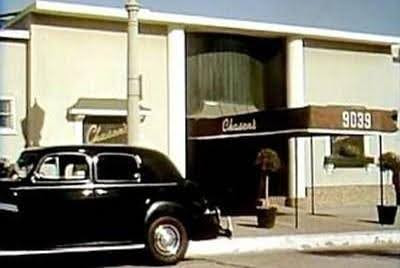 Black vintage car parked on the street in front of a building with a sign reading "Chanel" and the address 9039.