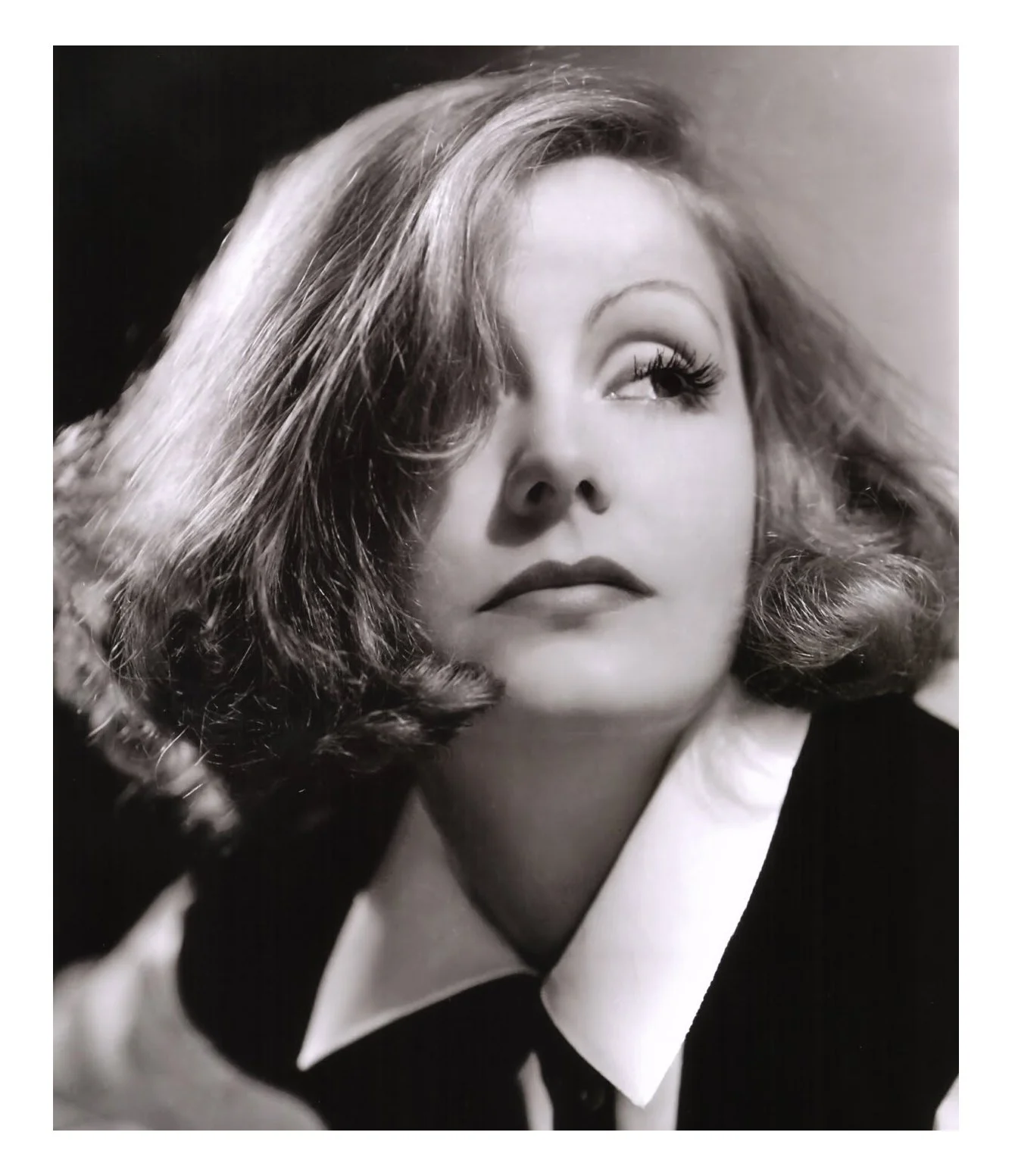 Black and white portrait of a woman with wavy hair looking upwards, wearing a collared shirt.