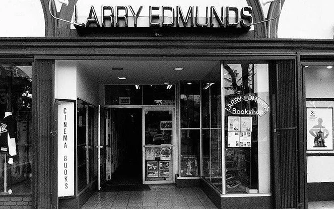 Exterior view of Larry Edmonds bookstore with neon sign and cinema books sign, glass entrance doors, and a poster on the right window.