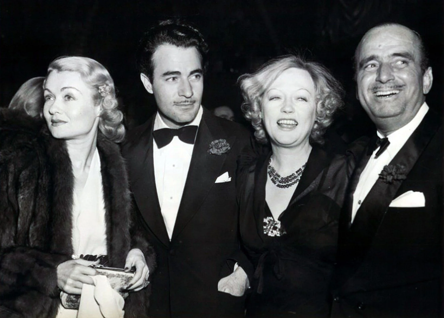 Black and white photo of four well-dressed people at a formal event, including two women and two men, smiling and posing for the camera.