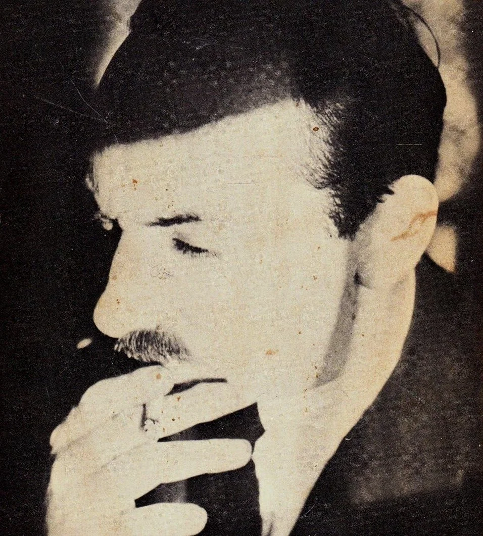 Black and white photograph of a man with his eyes closed, with the hand on his lips, wearing a ring and a mustache, in a contemplative pose.