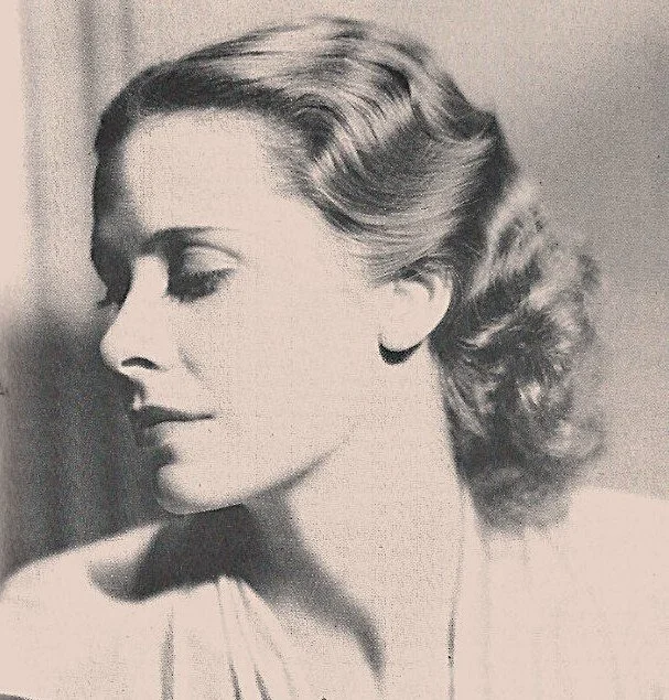 A black-and-white photo of a young woman with wavy hair styled in a vintage fashion, looking to her left with a calm expression.