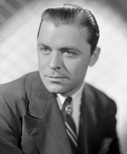 Black and white portrait of a man with slicked-back hair, wearing a suit and tie.
