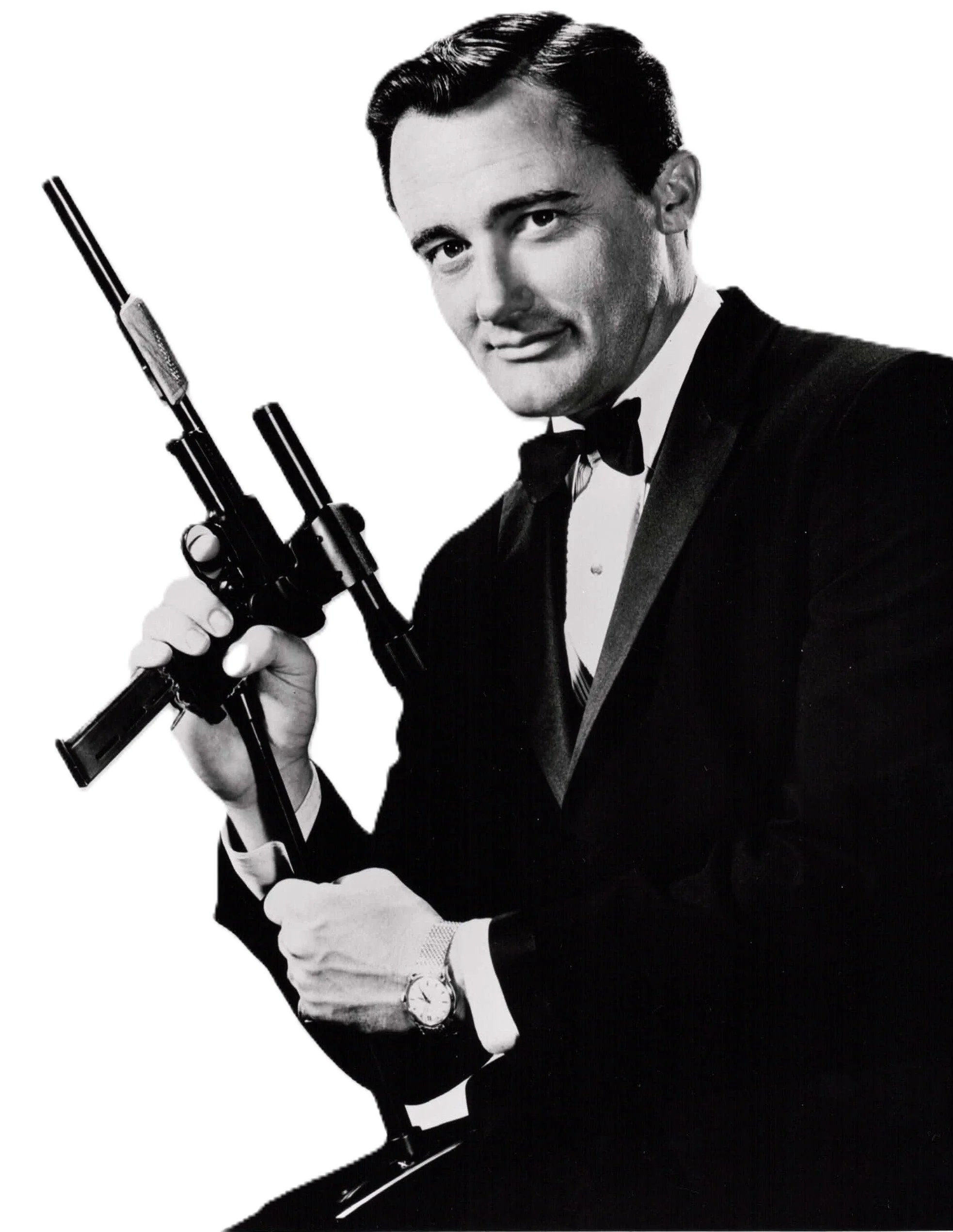Black and white image of a man in a tuxedo holding a gun, smiling and looking at the camera.
