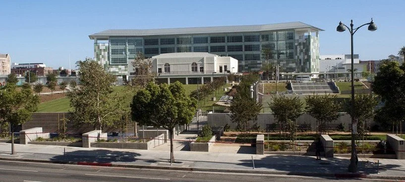 Modern glass building with landscaped steps and trees in front, street with lamp posts, clear blue sky
