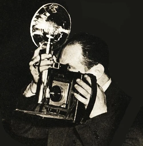 A woman taking a photograph with a camera, holding a mirror-like object in front of her face.