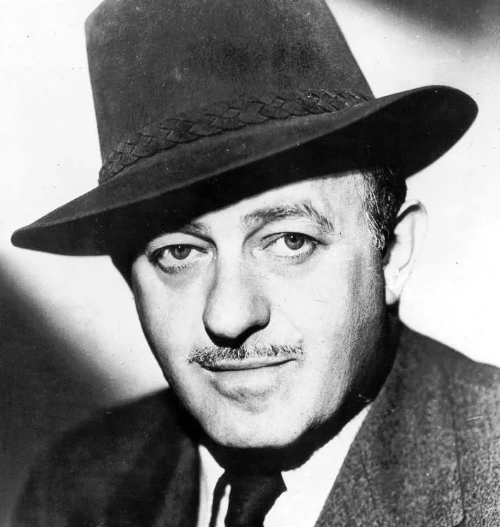 A black and white portrait of a man wearing a fedora hat, with a mustache, dressed in a suit and tie.