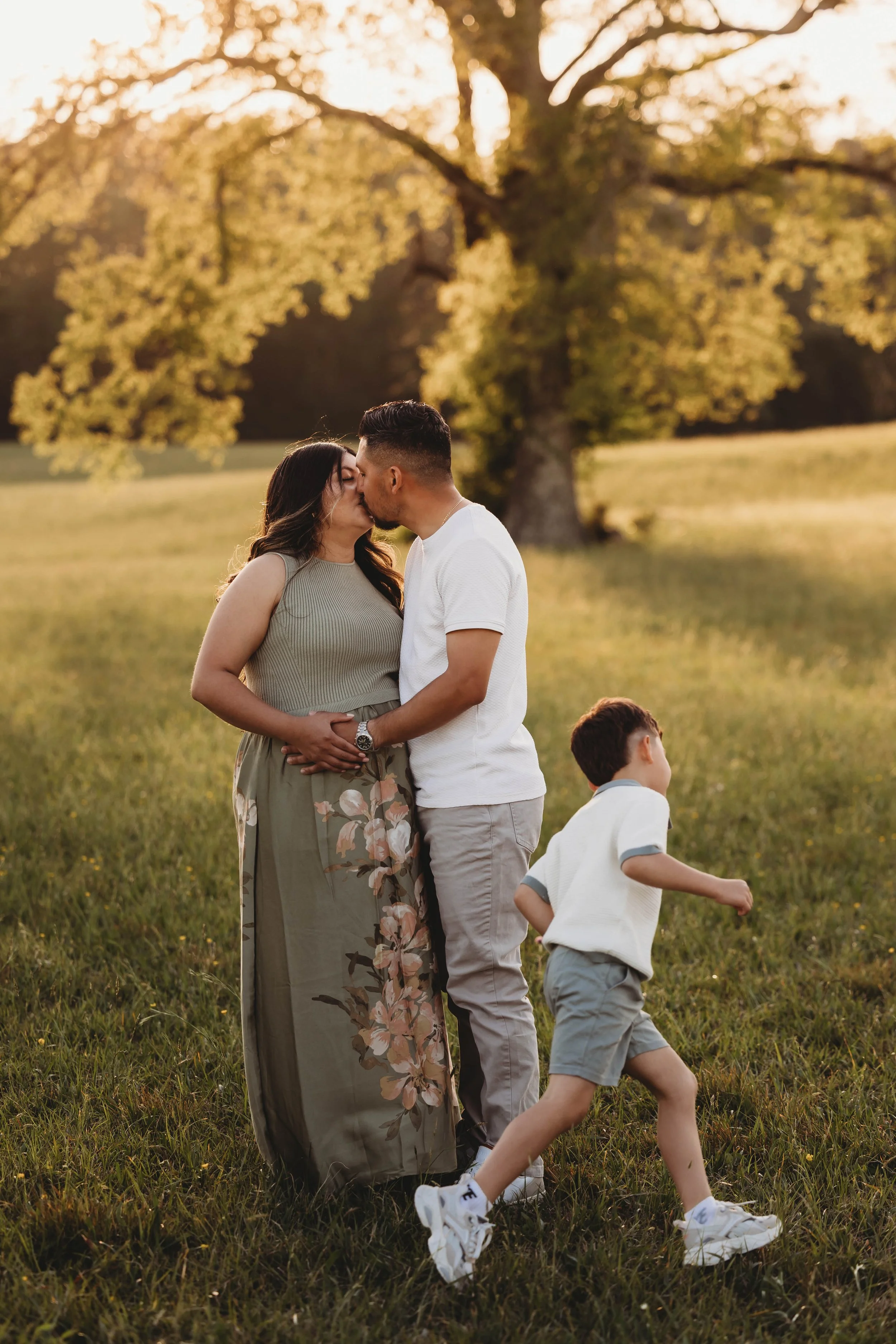 A couple shares a kiss outdoors in a field during sunset, with two children playing nearby.