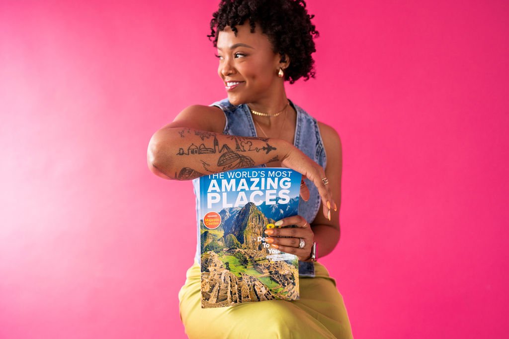 A woman holding a travel book titled 'The World's Most Amazing Places' against a pink background.