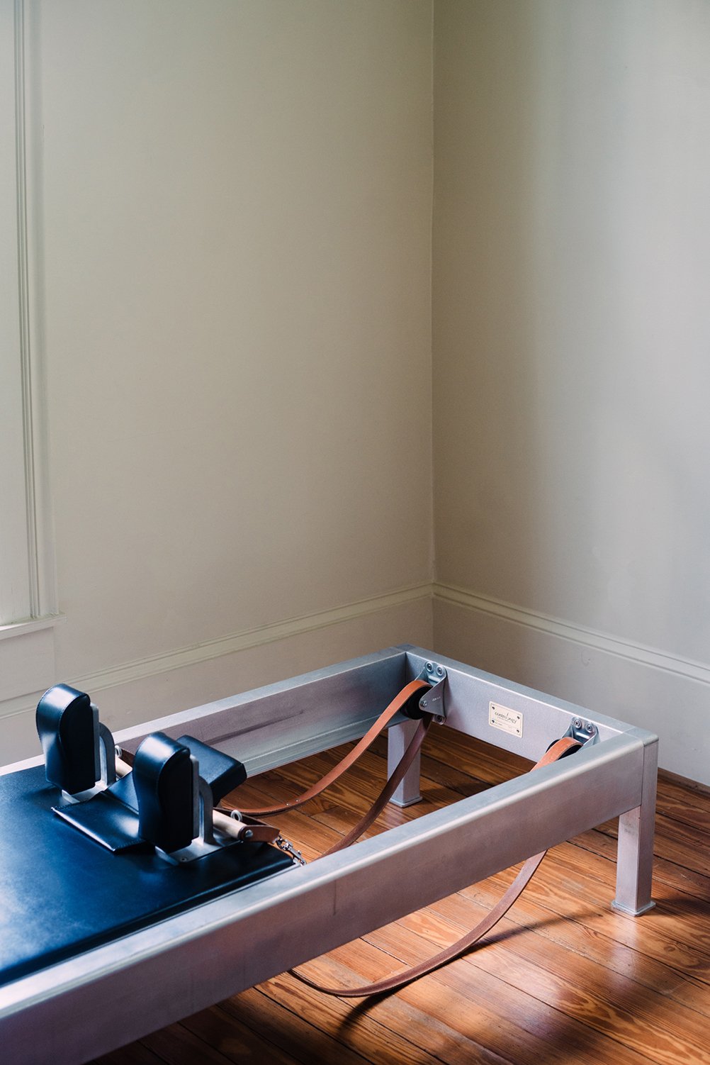 A chiropractic adjustment table with padded headrests, straps, and a metal frame, located in a room with beige walls and wooden flooring.