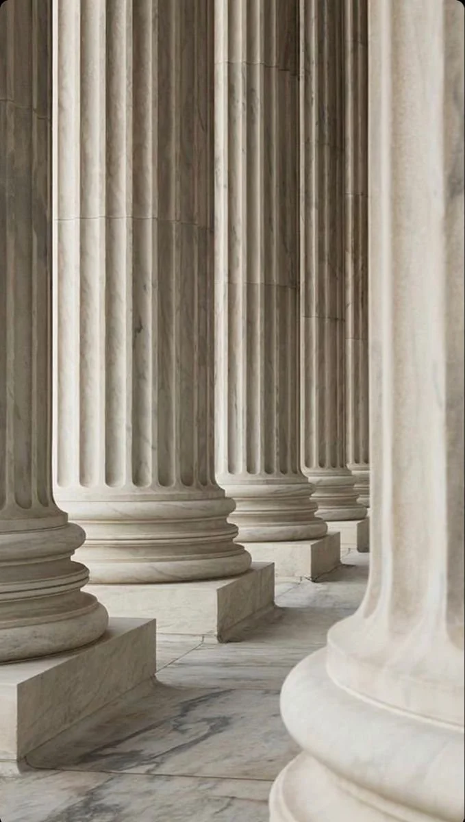 A row of marble columns in a neoclassical style, featuring fluted shafts and rounded bases, inside a grand building.