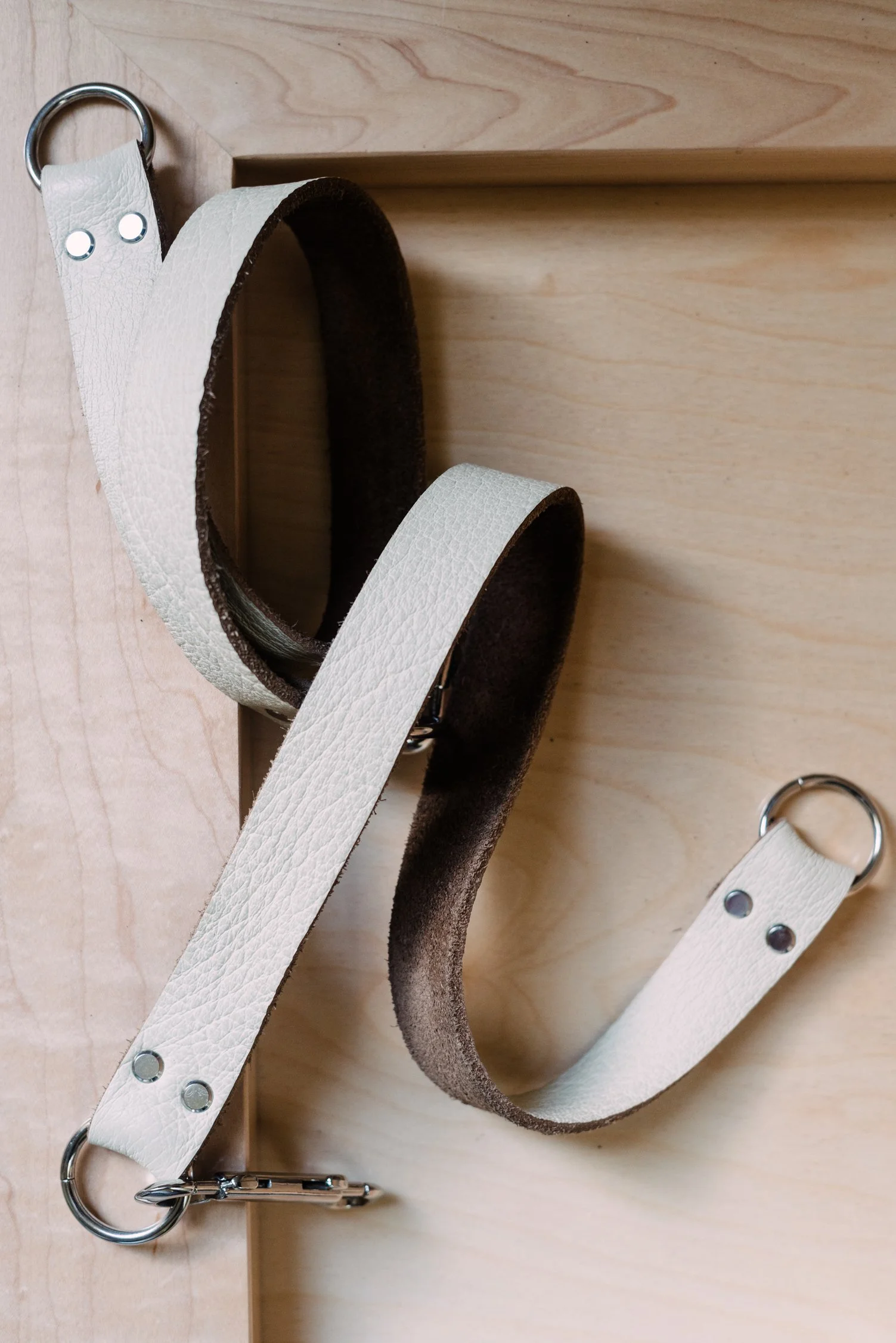 A leather belt with metal rings and fasteners, featuring a white textured outer surface and a dark interior, placed on a wooden surface.