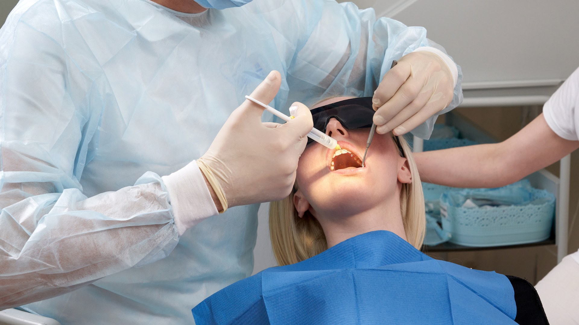 Dentist performing a dental procedure on a patient lying back in a dental chair, with dental tools and a syringe in use.