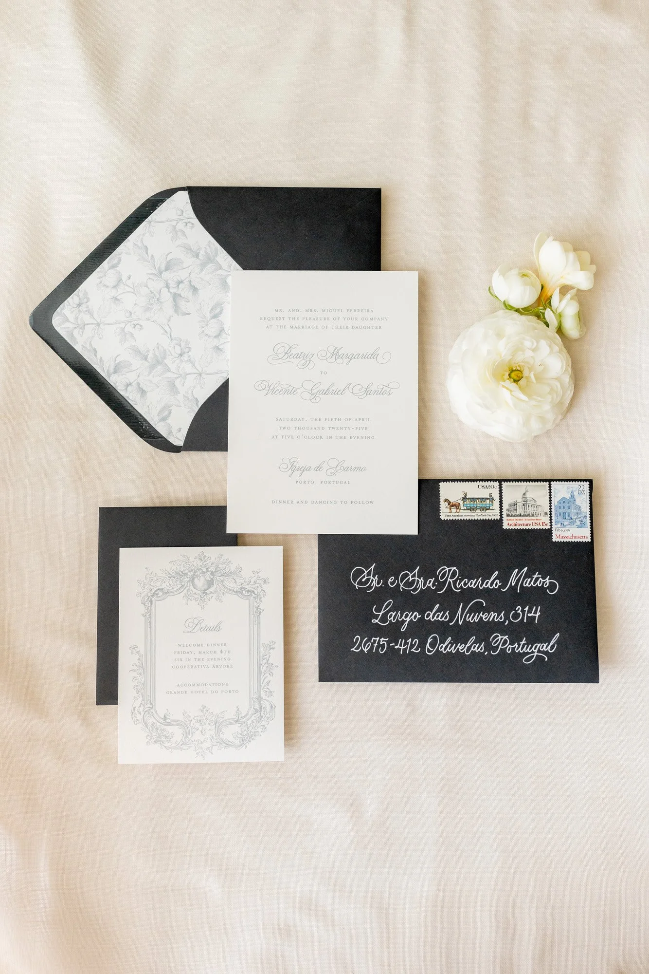 Elegant wedding invitation suite with an RSVP card, black envelope with white floral lining, and a black envelope with white calligraphy, accompanied by white flowers and vintage U.S. postage stamps.