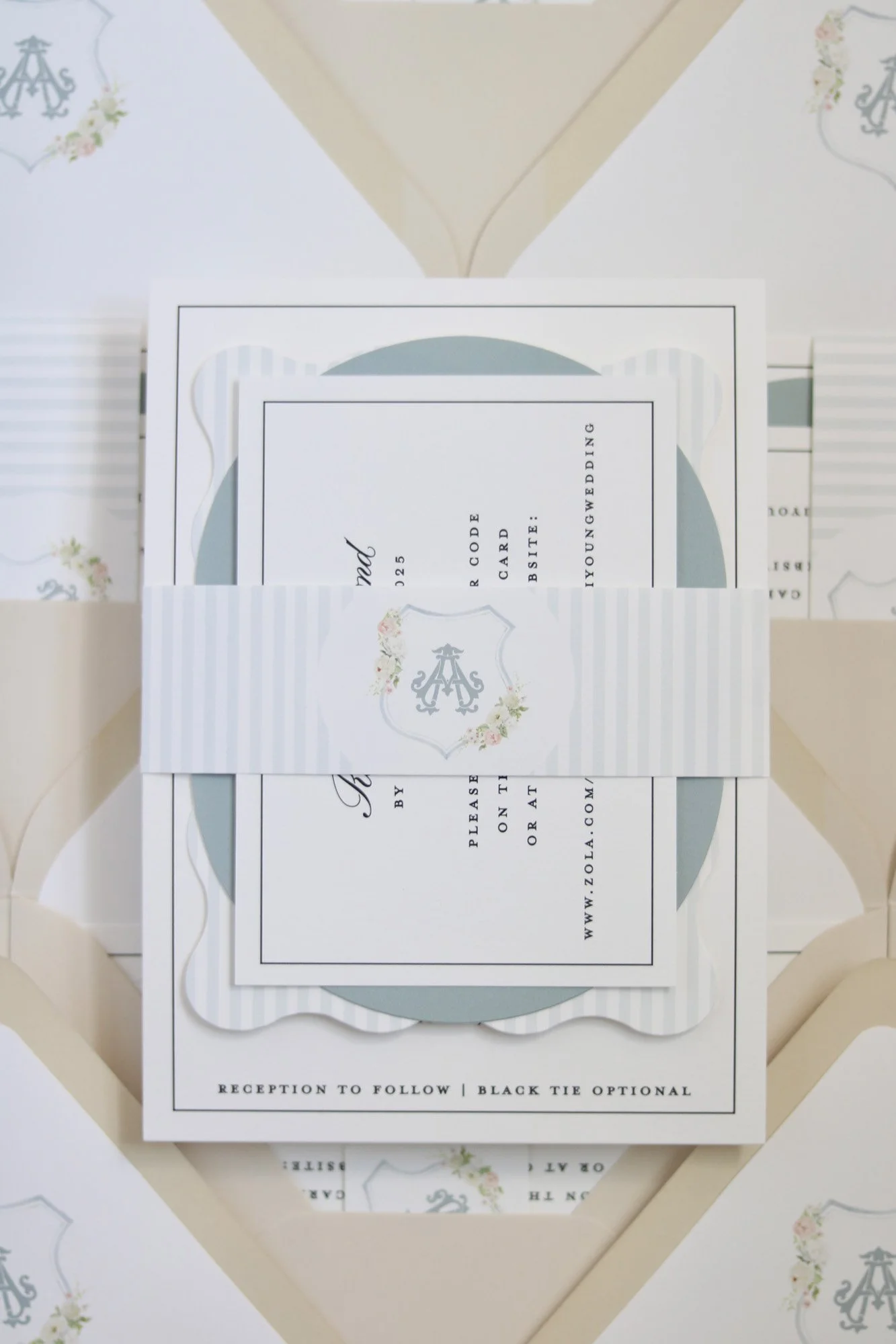 Wedding invitation cards with a light blue circular background, a white striped band, and elegant black text, with a monogrammed crest in gray and floral decorations.