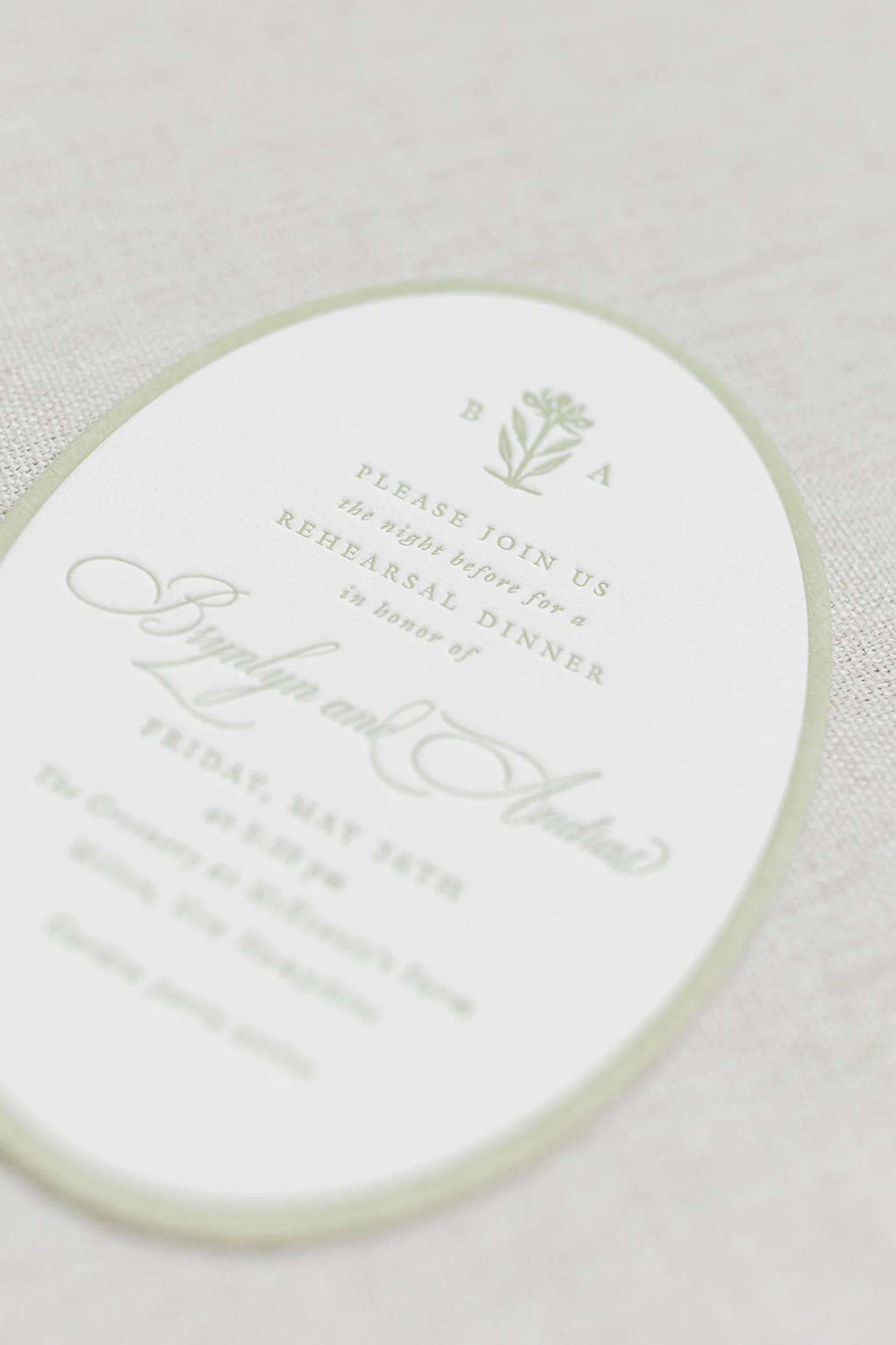 Close-up of a wedding or event card with a floral emblem at the top and elegant scripted and printed text.