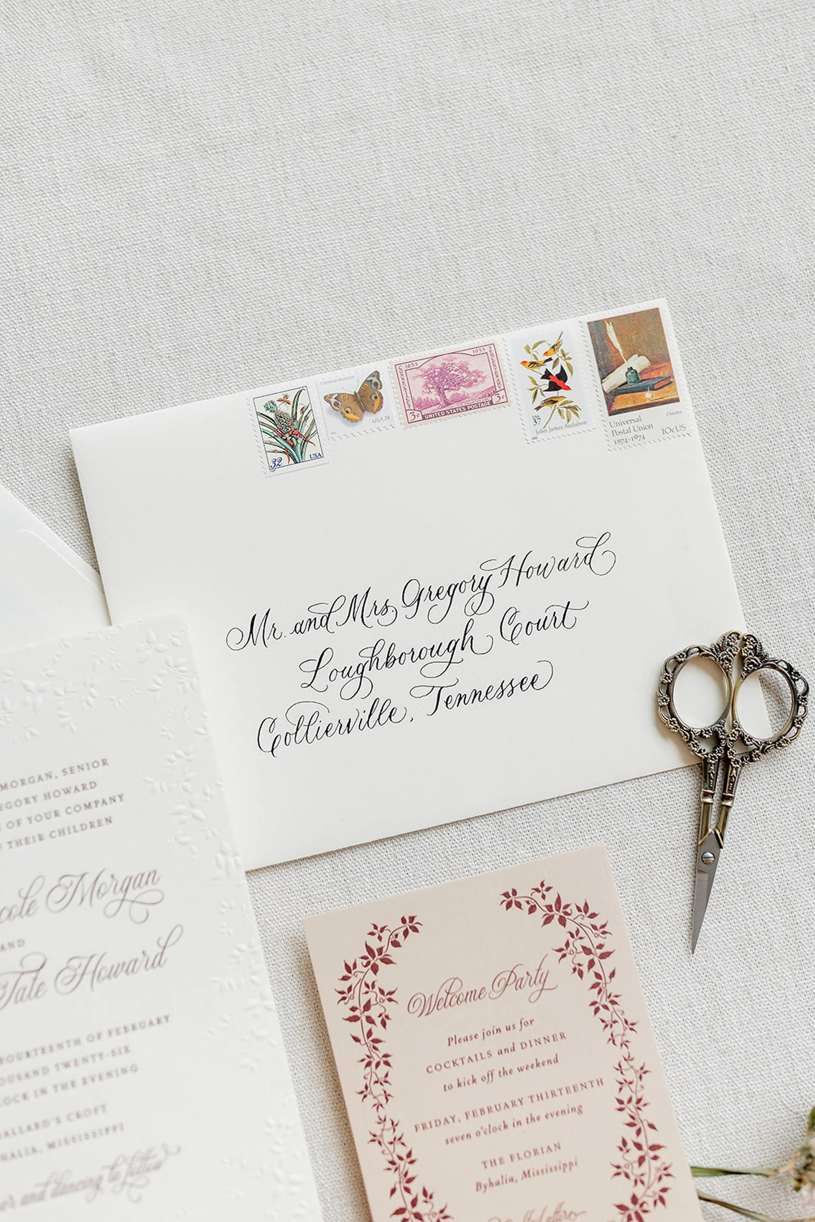 Wedding invitation with white background, decorated with red floral border, accompanied by a pair of vintage scissors and a floral spray.
