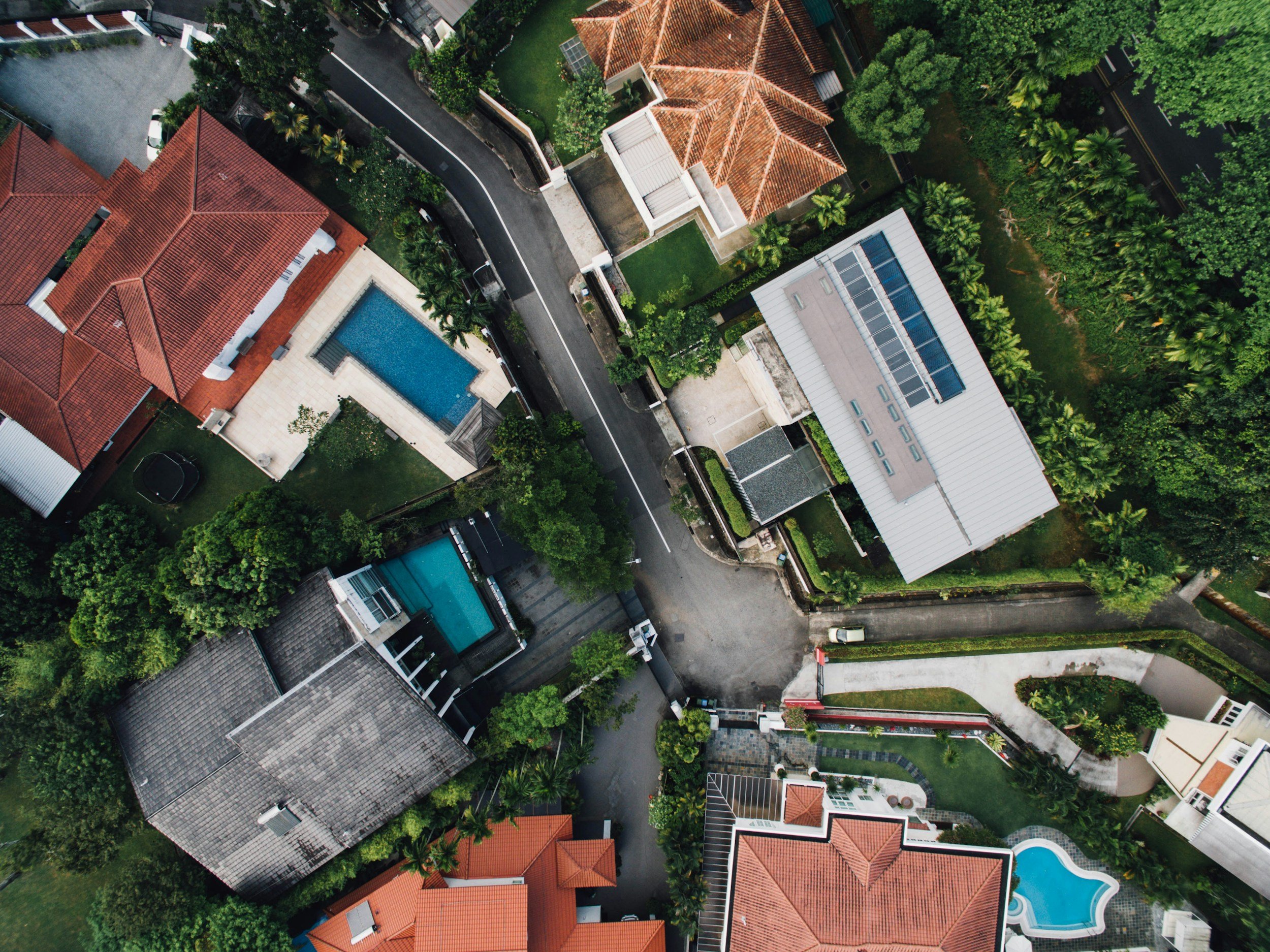 An aerial view of a residential neighborhood showing rooftops, a swimming pool, trees, and streets.